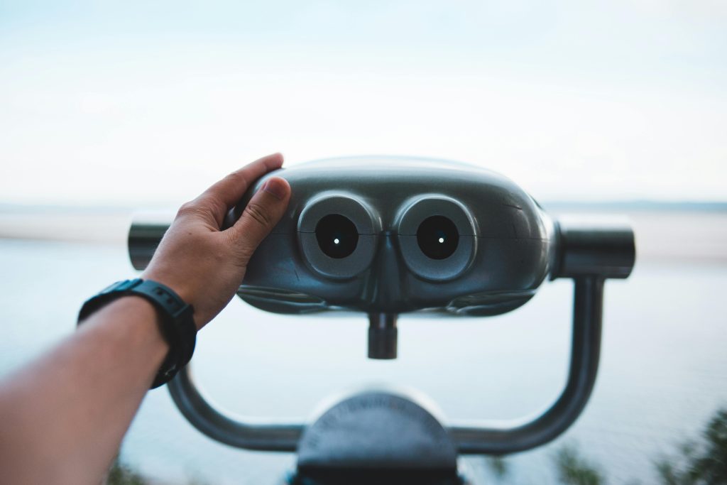 A person explores the coastline view through metal binoculars. Serene and perfect for travel theme.