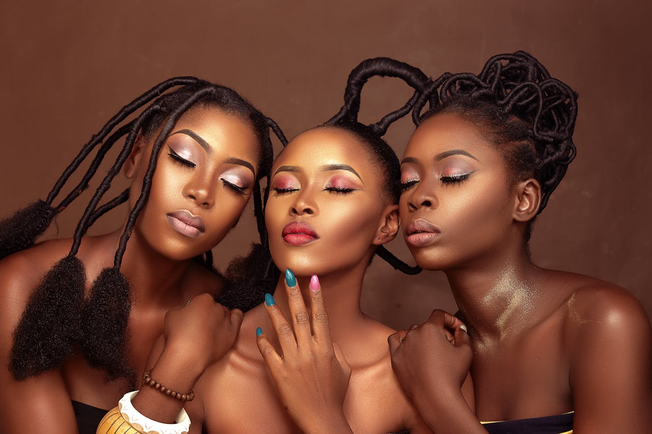 Close-up portrait of three African women with elegant hairstyles and makeup, showcasing diverse beauty and culture.